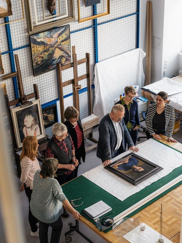 Foto: Mehrere Erwachsene blicken auf ein Kunstwerk auf einem Tisch.