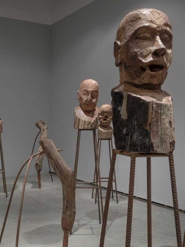 Installation aus hölzernen Skulpturen, die auf Sockeln aus geriffelten Metallstangen stehen.