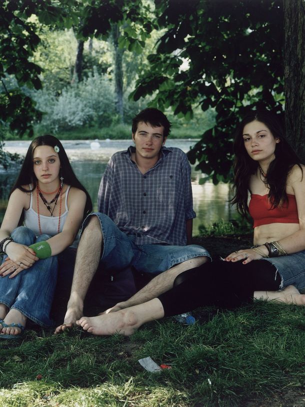 Photography: Four young people are sitting or lying in summer clothes in a park. They are looking directly at the camera.