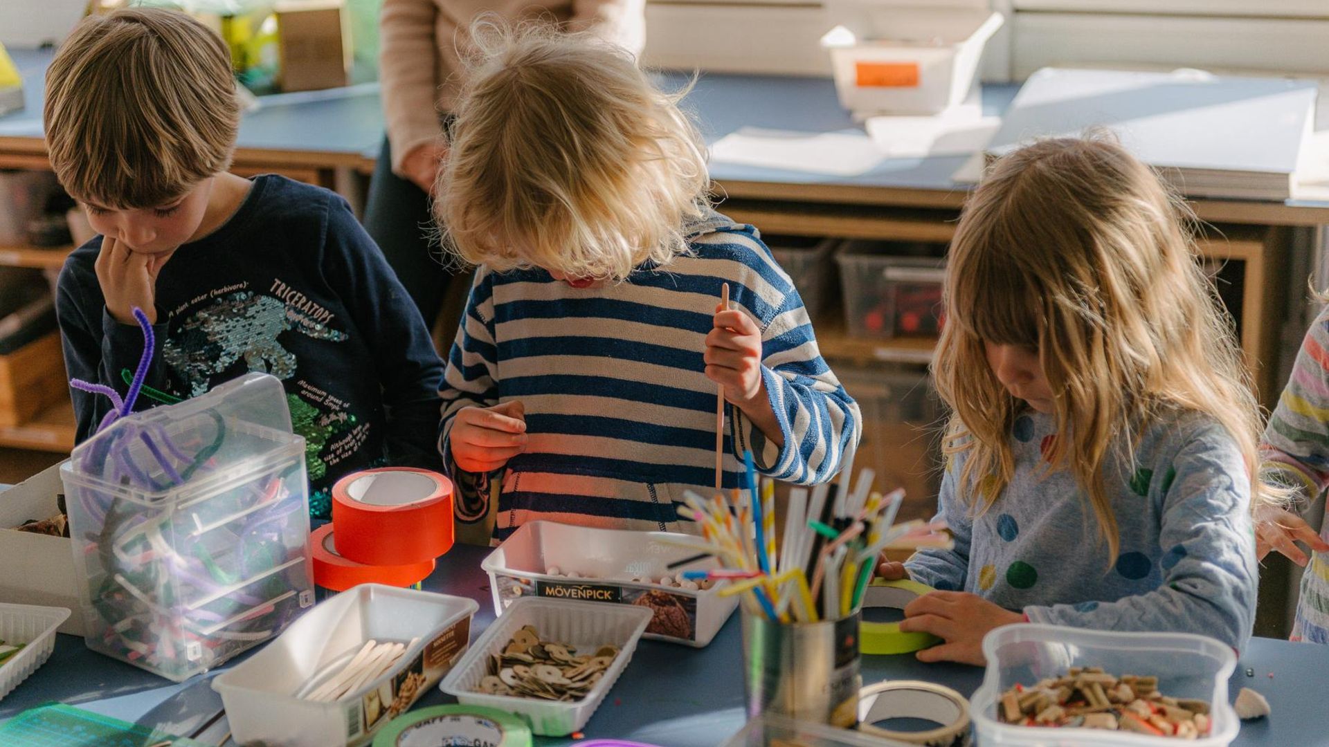 Foto: Drei Kinder spielen mit Bastelmaterialien auf dem Tisch vor ihnen.