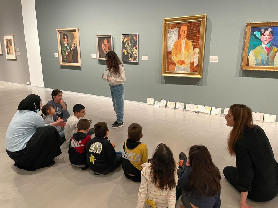 Kinder sitzen auf dem Boden im Museum vor Bildern