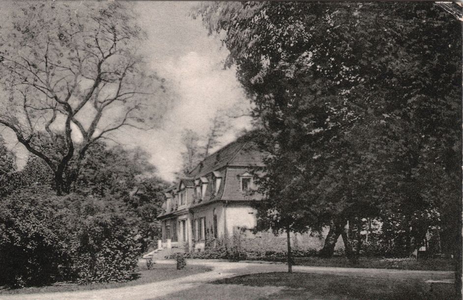 Schwarz-Weiß-Fotografie: Seitenansicht eines Gutshaus umgeben von Bäumen