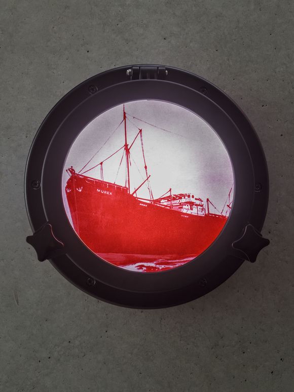 Photo: View of a round window (porthole) in which a large ship can be seen in bright red colour on a white and pink background. ‘Murex’ is written in capital letters on the bow of the ship.