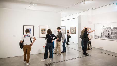 ein Schüler steht mit einer Menschengruppe vor einem Bild der Dauerausstellung. Man sieht ihre Rückenansichten. Sie sind im Gespräch über die Kunst. 