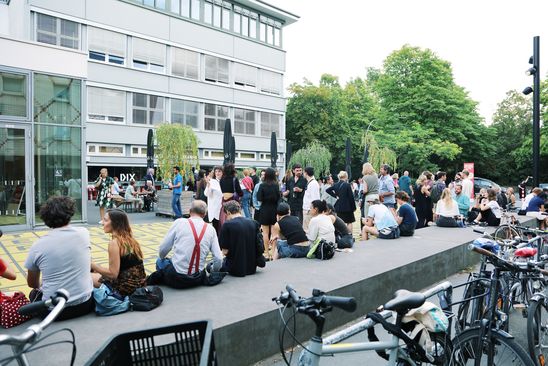 Einige Menschen sitzen in kleineren Gruppen auf einer steinernen Plattform vor dem Museum und unterhalten sich.