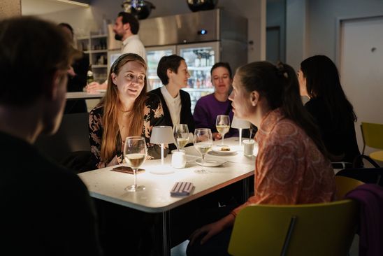 Foto: Eine Gruppe Menschen sitzt abends im Museumscafé der Berlinischen Galerie um einen Tisch herum.