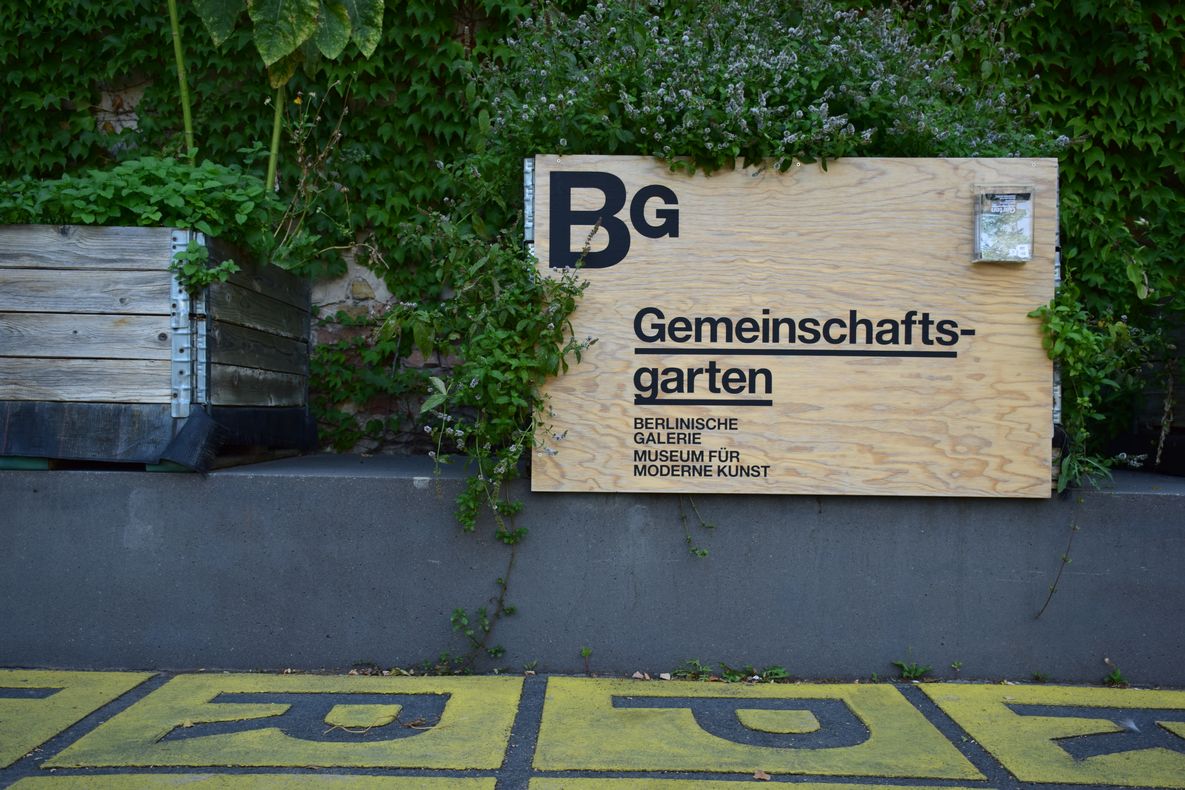 Foto: Hochbeete vor dem gelben Buchstabenfeld und ein Schild mit der Aufschrift: BG Gemeinschaftsgarten.