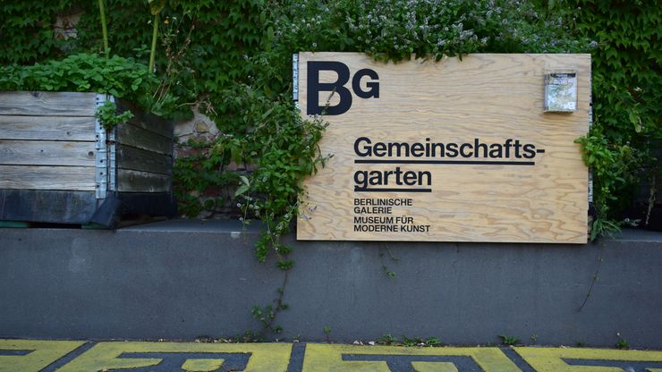 photo: raised beds infront of the yellow letterfield and a sign which has "BG Gemeinschaftsgarten" (community garden) written on it.
