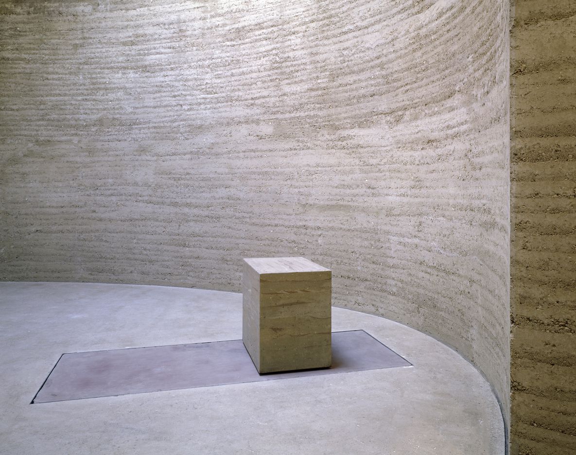 Foto: Innenansicht eines runden, minimalistischen Innenraums aus Lehm mit einem kleinen Altar, der ebenfalls aus Lehm besteht.