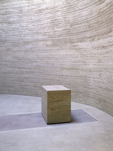 Foto: Innenansicht eines runden, minimalistischen Innenraums aus Lehm mit einem kleinen Altar, der ebenfalls aus Lehm besteht.