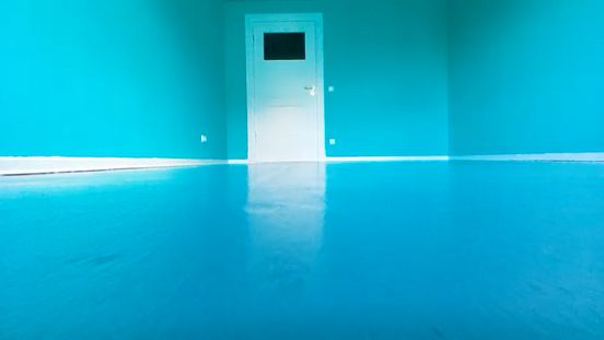 Film still: A view into a room with a bright aquamarine-coloured floor and walls, and a white door with a dark glass pane.