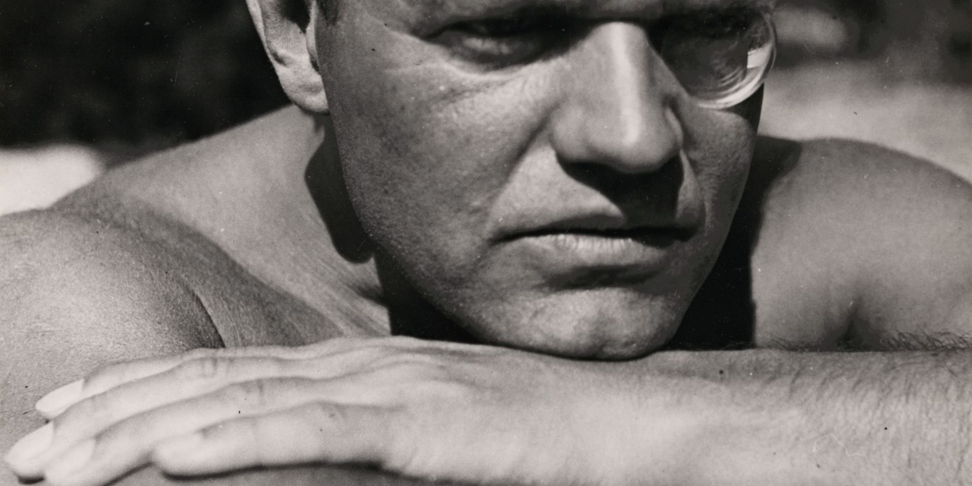 Black-and-white photograph by Raoul Hausmann, who is looking past the viewer into the distance with his head resting on his folded arms, his left eye round.