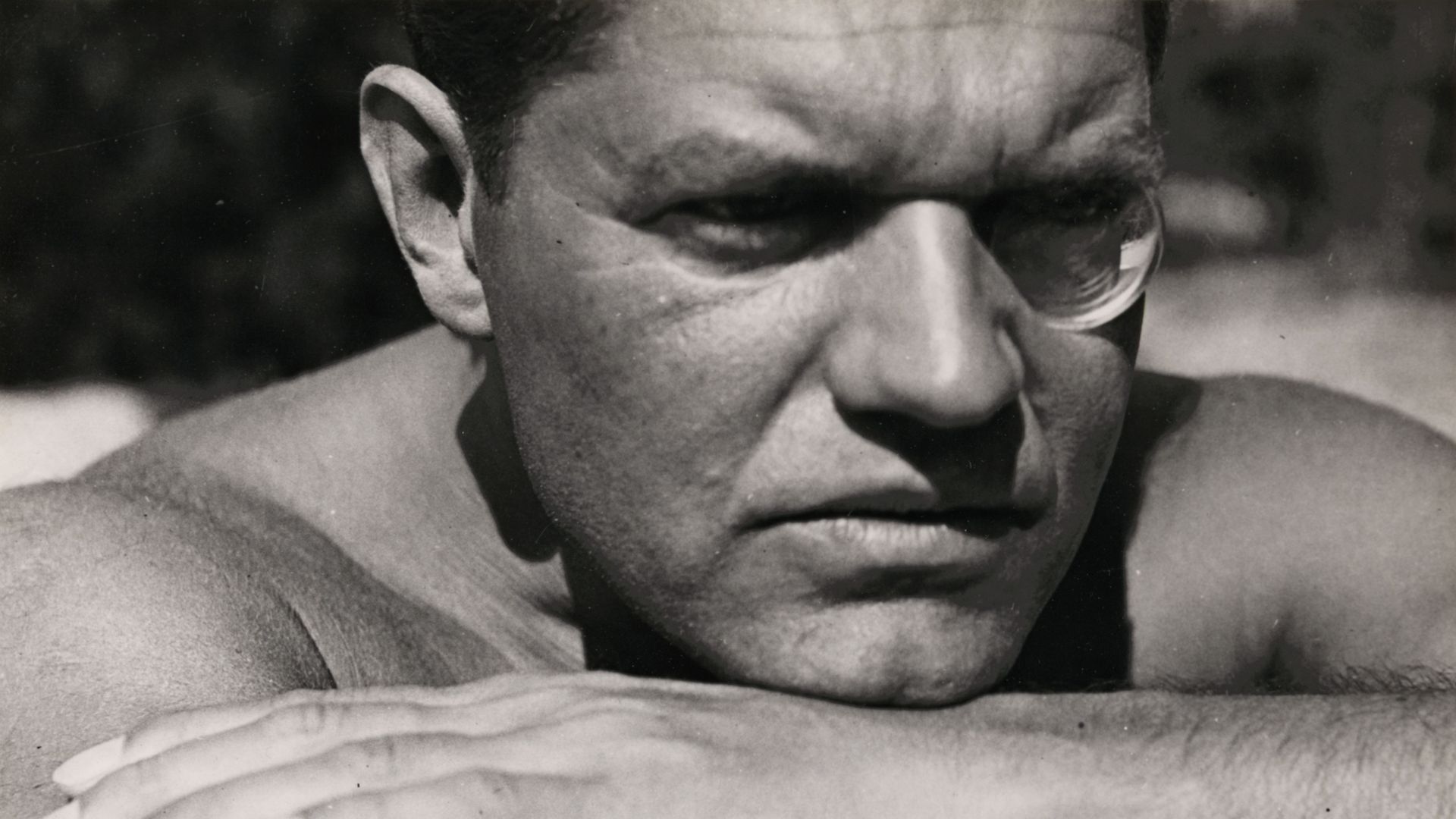 Black-and-white photograph by Raoul Hausmann, who is looking past the viewer into the distance with his head resting on his folded arms, his left eye round.