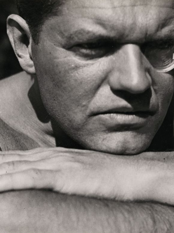 Black-and-white photograph by Raoul Hausmann, who is looking past the viewer into the distance with his head resting on his folded arms, his left eye round.