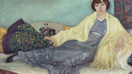 Gemälde einer Frau, die auf einem Sofa sitzt. Sie trägt ein fließendes blaues Kleid und ein gelbes Tuch über den Schultern. Der Hintergrund ist türkisfarben, und um sie herum liegen gemusterte Kissen und Teppiche.