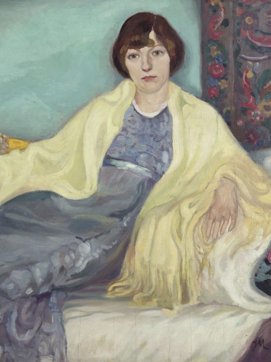 Painting of a woman reclining on a sofa. She wears a flowing blue dress and a yellow shawl draped over her shoulders. The background is turquoise, with patterned pillows and carpets surrounding her. 