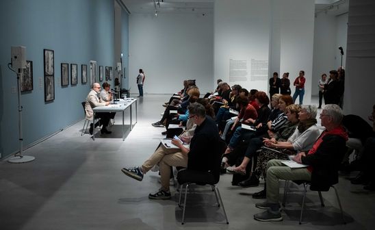 Foto: Blick auf die Pressekonferenz der beiden Ausstellungen. Viele Personen sitzen vor den beiden Redner*innen Thomas Köhler und Katia Reich in Stuhlreihen. 