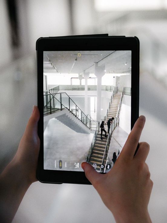 Photo: Person holding a tablet. It shows a photograph of the stairs in the museum.