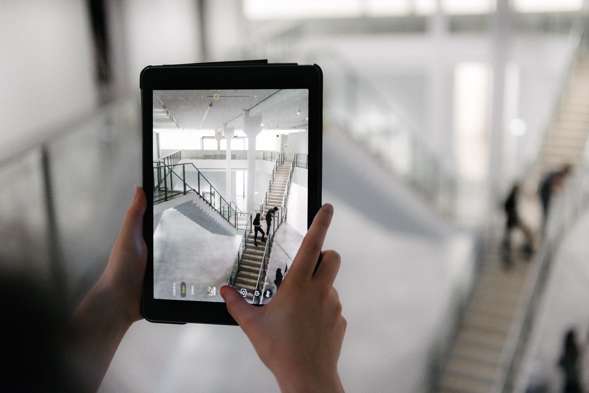 Berlinische-Galerie-Museum-Berlin-Architektur Foto: Besucher:in hält ein Tablet in der Hand. Es zeigt die Aufnahme eines Fotos von der Treppe im Museum.