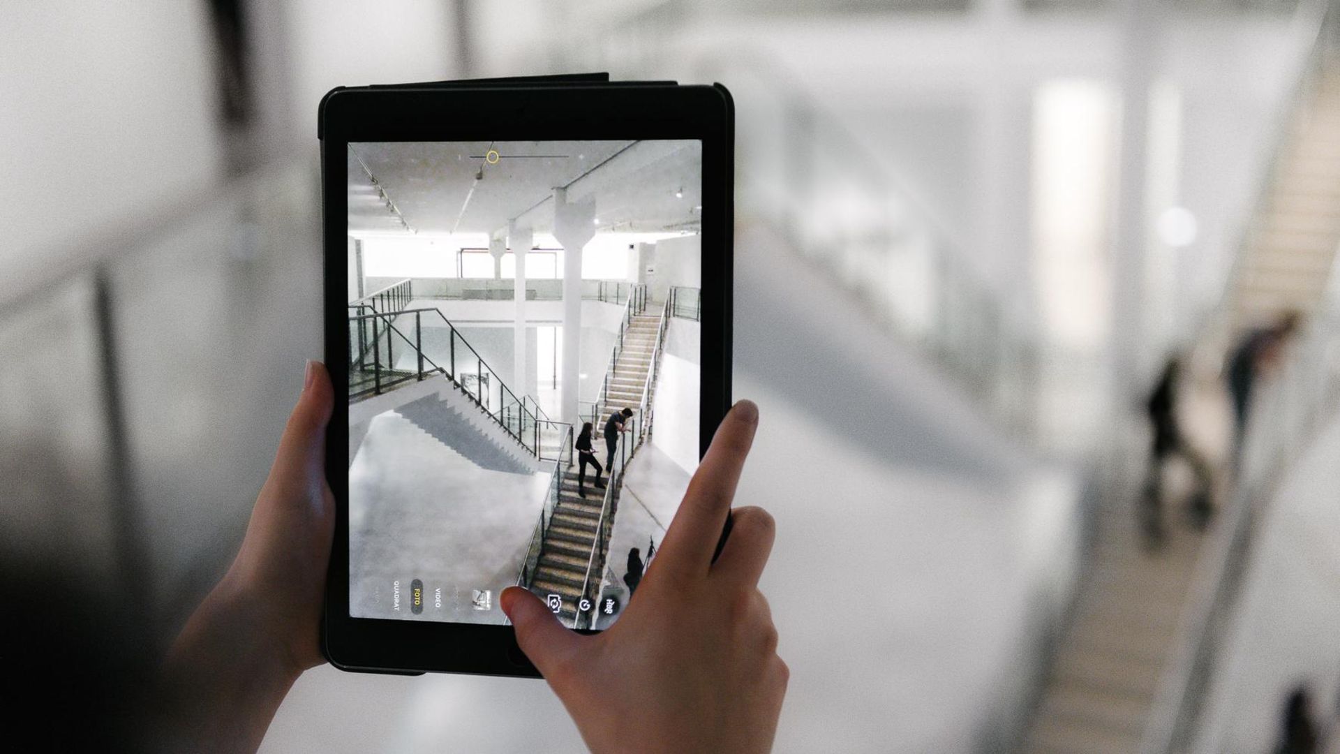 Photo: Person holding a tablet. It shows a photograph of the stairs in the museum.