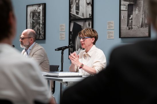 Foto: Katia Reich und Thomas Köhler an einem Tisch sitzend bei der Pressekonferenz. Hinter ihnen sind Schwarz-Weiß-Fotografien von Akinbode Akinbiyi zu sehen.