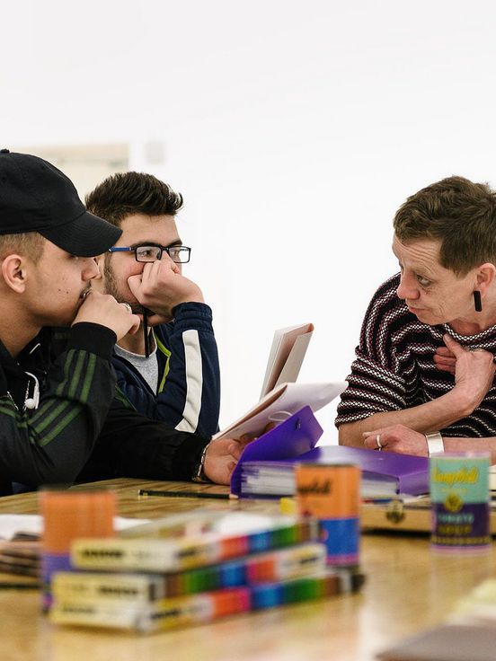 Foto: Zwei Jugendliche und eine erwachsene Person sitzen an einem Tisch und unterhalten sich.