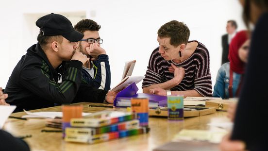 Foto: Zwei Jugendliche und eine erwachsene Person sitzen an einem Tisch und unterhalten sich.