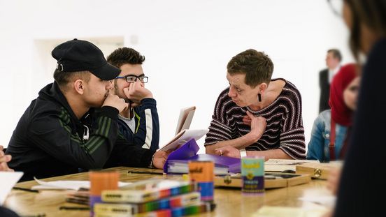 Foto: Zwei Jugendliche und eine erwachsene Person sitzen an einem Tisch und unterhalten sich.