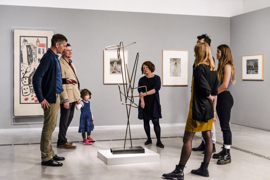 Photo: Adults and a child during a guided tour. They are standing around a sculpture.