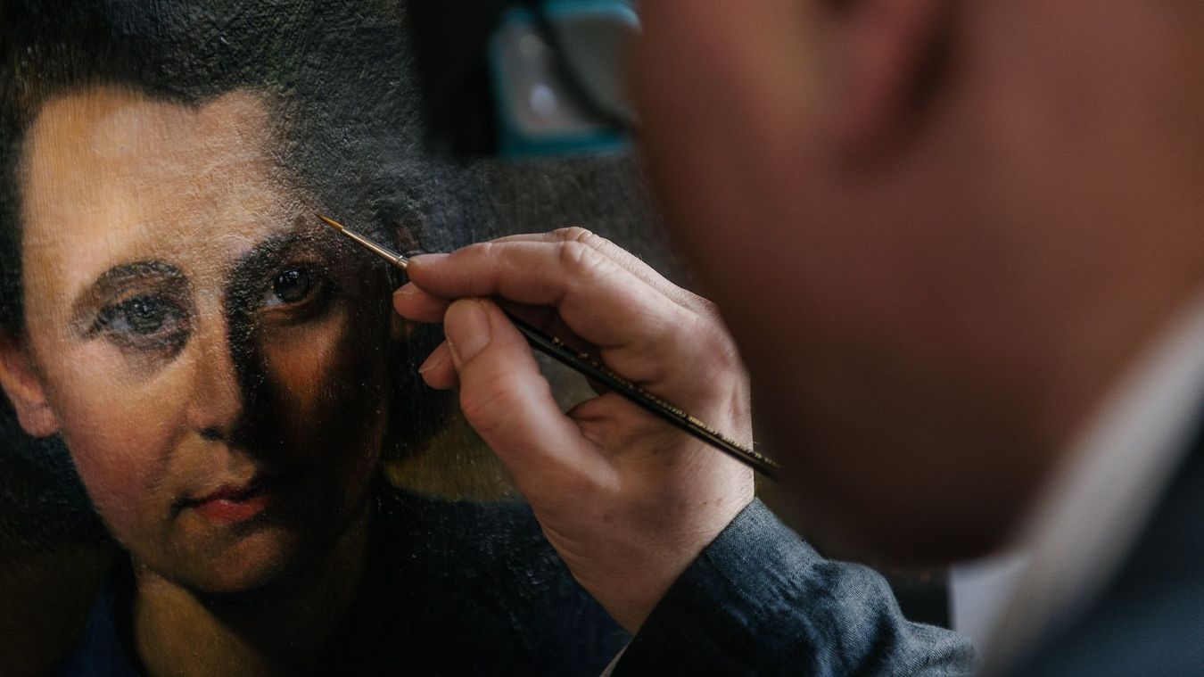 Photo: Person holding a brush in front of a painting.