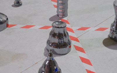 Filmstill: Verschiedene Metallformen stehen auf dem Boden, der durch Absperrmarkierungen unterteilt wird