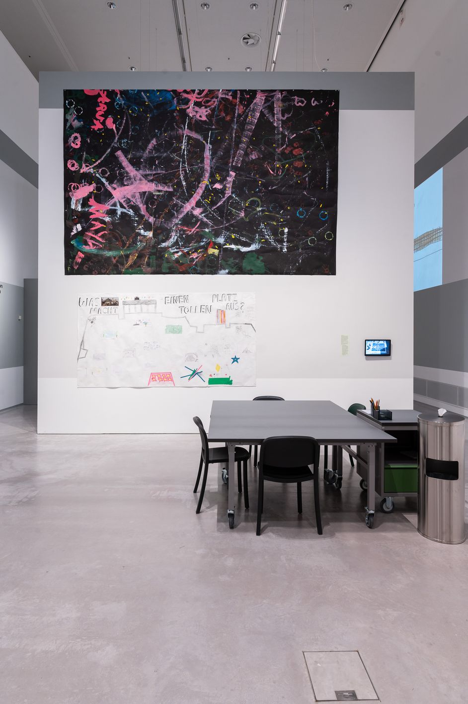 Ein großer Raum mit Tischen, Stühlen und einem großen Kunstwerk aus Papier an der Wand.