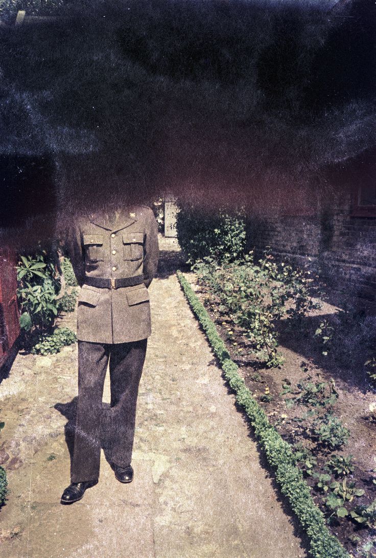 Carla Åhlander, Untitled, 2025, 35 mm colour negative Photograph: Colour negative showing a person in uniform on a path lined with flowerbeds. The person's head and the entire upper half of the photograph are darkened and therefore obscured.