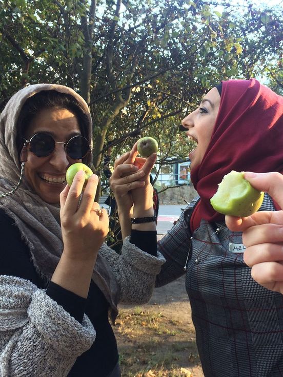 Foto: Zwei fröhliche Frauen halten kleine Äpfel. Eine weitere Hand hält einen angebissenen Apfel ins Bild.