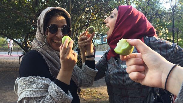 Foto: Zwei fröhliche Frauen halten kleine Äpfel. Eine weitere Hand hält einen angebissenen Apfel ins Bild.