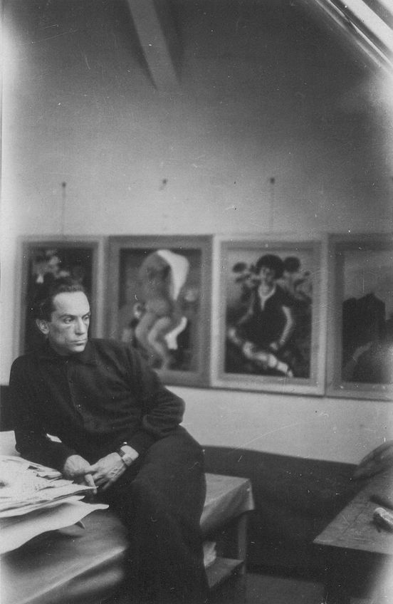 Black and white photograph: Richard Ziegler sits in his studio, his gaze seemingly lost in thought. The background shows framed paintings.