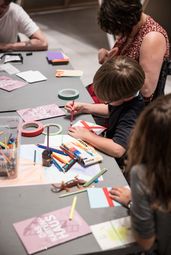 Foto: Eine erwachsene Person und Kinder sitzen an einem Tisch und basteln.