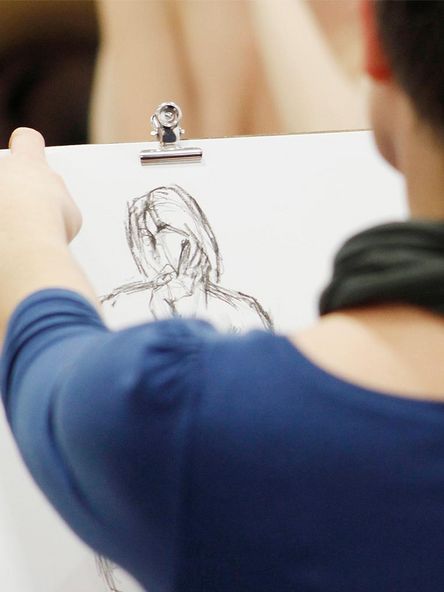 Foto: Person hält ein Klemmbrett und zeichnet eine Figur auf Papier.