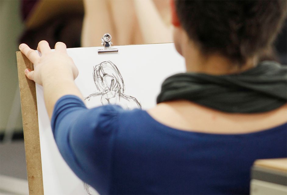Foto: Person hält ein Klemmbrett und zeichnet eine Figur auf Papier.