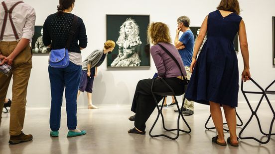 Foto: Menschen stehen und sitzen im Ausstellungsraum und schauen auf eine Fotografie.