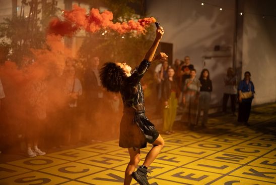Photo: Mélissa Guex in motion, holding a Bengalo, during her performance, pictured here on the forecourt of the Berlinische Galerie.