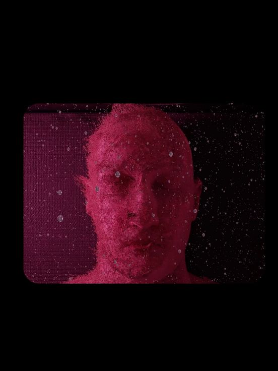 Video still: Frontalansicht einer Person mit geschlossenen Augen in einer Art Flüssigkeit. Das Still zeigt die selbe Ansicht zweimal nebeneinander und pink eingefärbt. Um beide Fenster herum liegt ein schwarzer Rahmen.