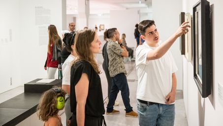 ein Schüler zeigt einer Besucher*innen etwas in dem Bild, über das er während der Kunstgespräche in der Dauerausstellung spricht