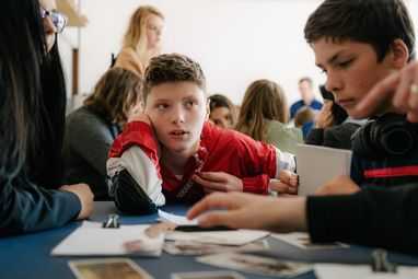 Foto: Schüler*innen sitzen um einen Tisch mit Materialien und diskutieren miteinander