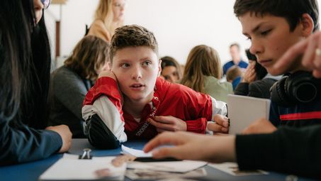 Photo: Pupils sitting around a table with materials and discussing with each other.