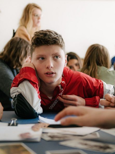 Foto: Schüler*innen sitzen um einen Tisch mit Materialien und diskutieren miteinander