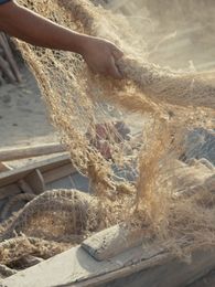 Filmstill: Nahaufnahme eines Fischerei-Netzes, das von zwei Personen gehalten wird.
