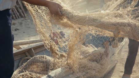 Film still: A close-up of a fishing net being held by two people.