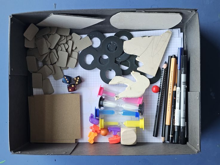 Blick in einer Materialkiste mit Stiften, Papieren und bunten Sanduhren