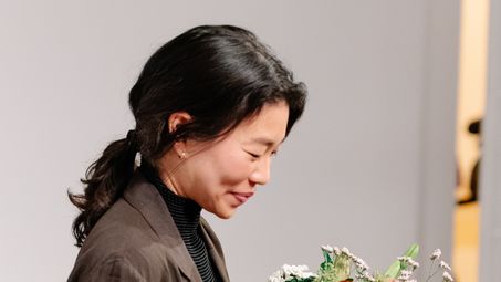 Photo: Jeewi Lee after the awards ceremony, holding her certificate and a bouquet of flowers.